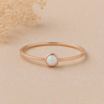 Minimalist Thin Rose gold stacker ring with a small round bezel set lab-created white opal stone on a beige background