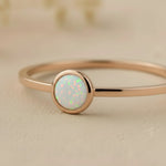 Rose gold ring with a round opal stone on a beige background