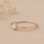 side view of a Minimalist Rose Gold Stacker Ring with a dainty round lab created white opal stone on a beige background