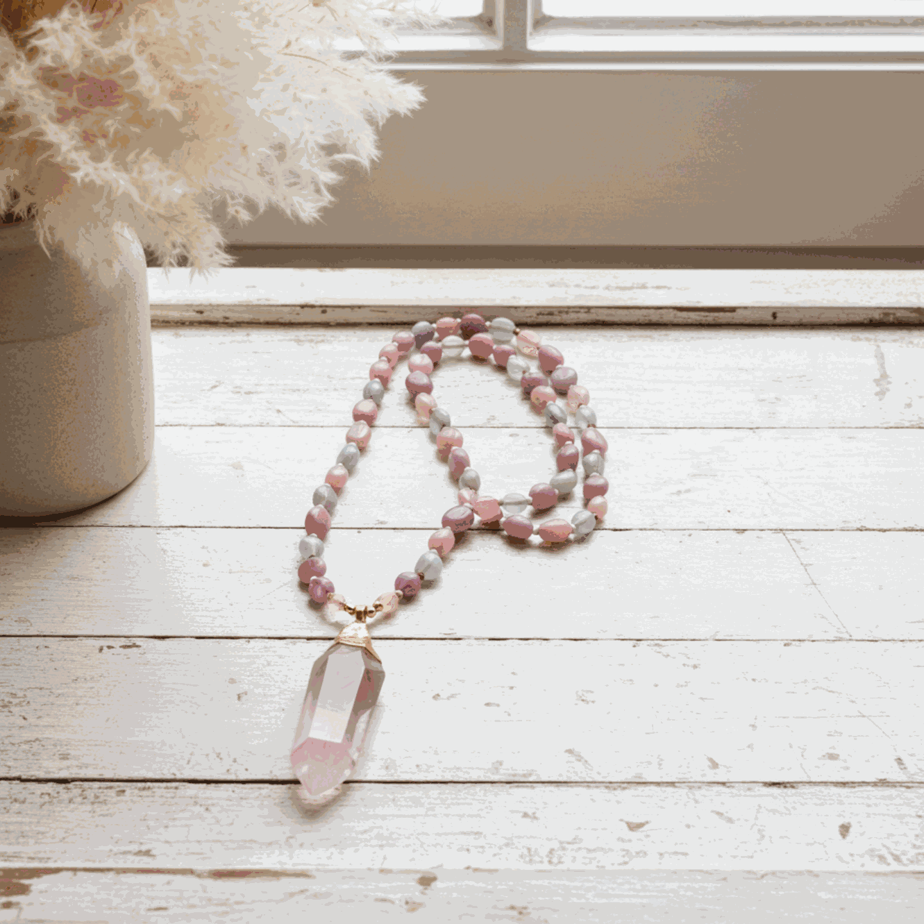 Beaded necklace with a pink crystal pendant on a wooden surface