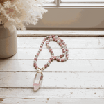 Beaded necklace with a pink crystal pendant on a wooden surface