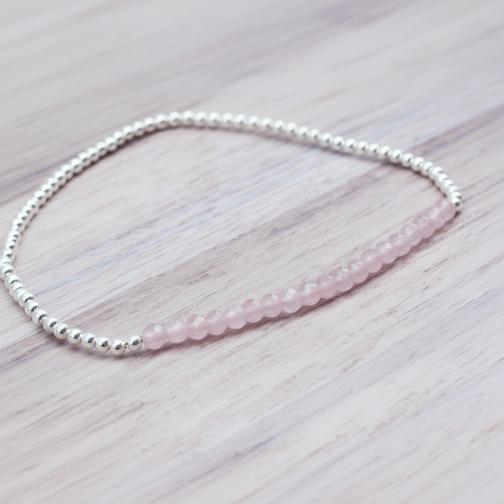 Beaded bracelet with pink rose quartz beads and silver beads on a light wooden surface