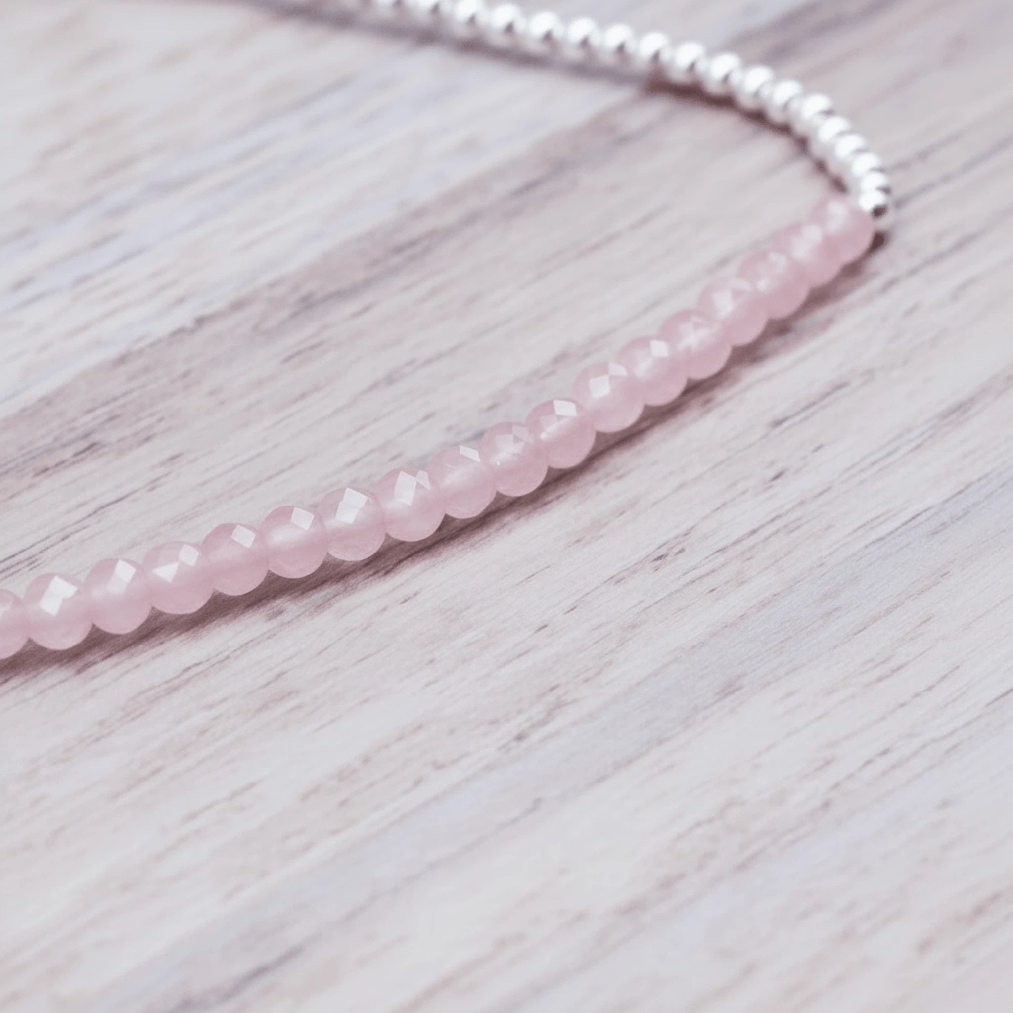 close up of a sterling silver Beaded bracelet with pink faceted rose quartz gemstone beads on a light wooden surface