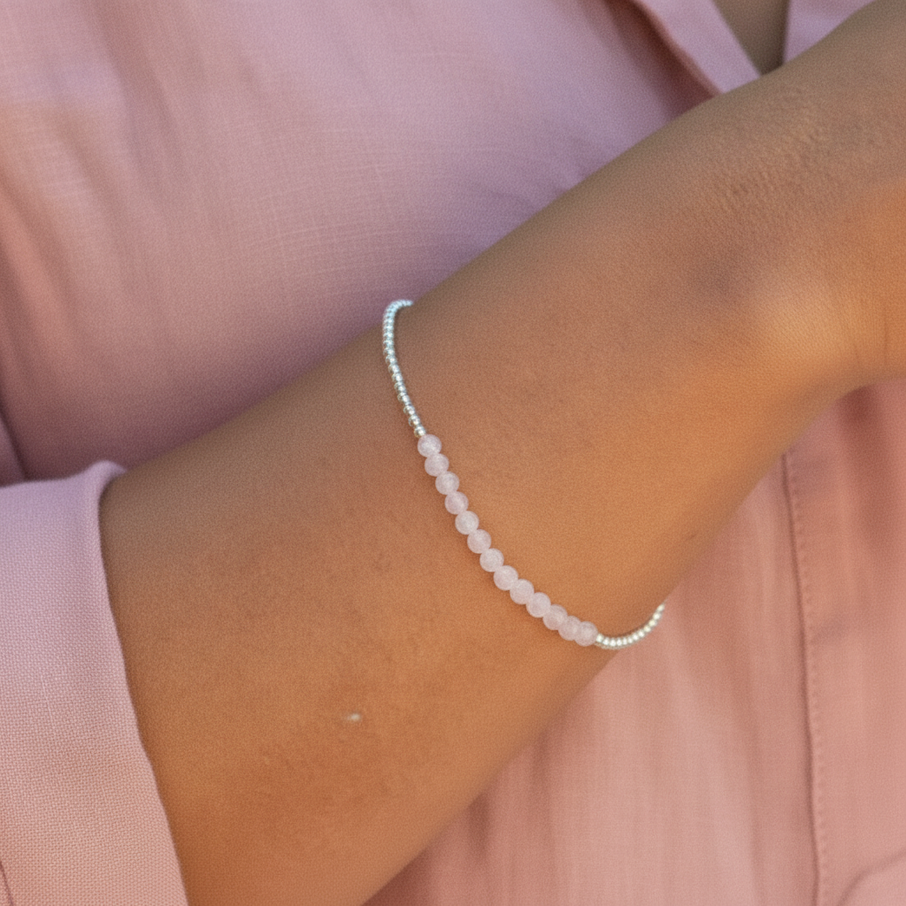 Close-up of a wrist wearing a beaded rose quartz bracelet against a pink background