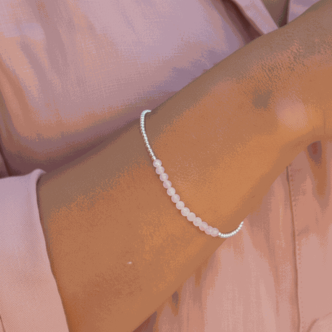 Close-up of a wrist wearing a beaded rose quartz bracelet against a pink background