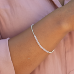 Close-up of a wrist wearing a beaded rose quartz bracelet against a pink background