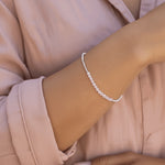lifestyle image of a woman wearing a light pink shirt and a a sterling silver beaded bracelet with natural light pink rose quartz gemstones.