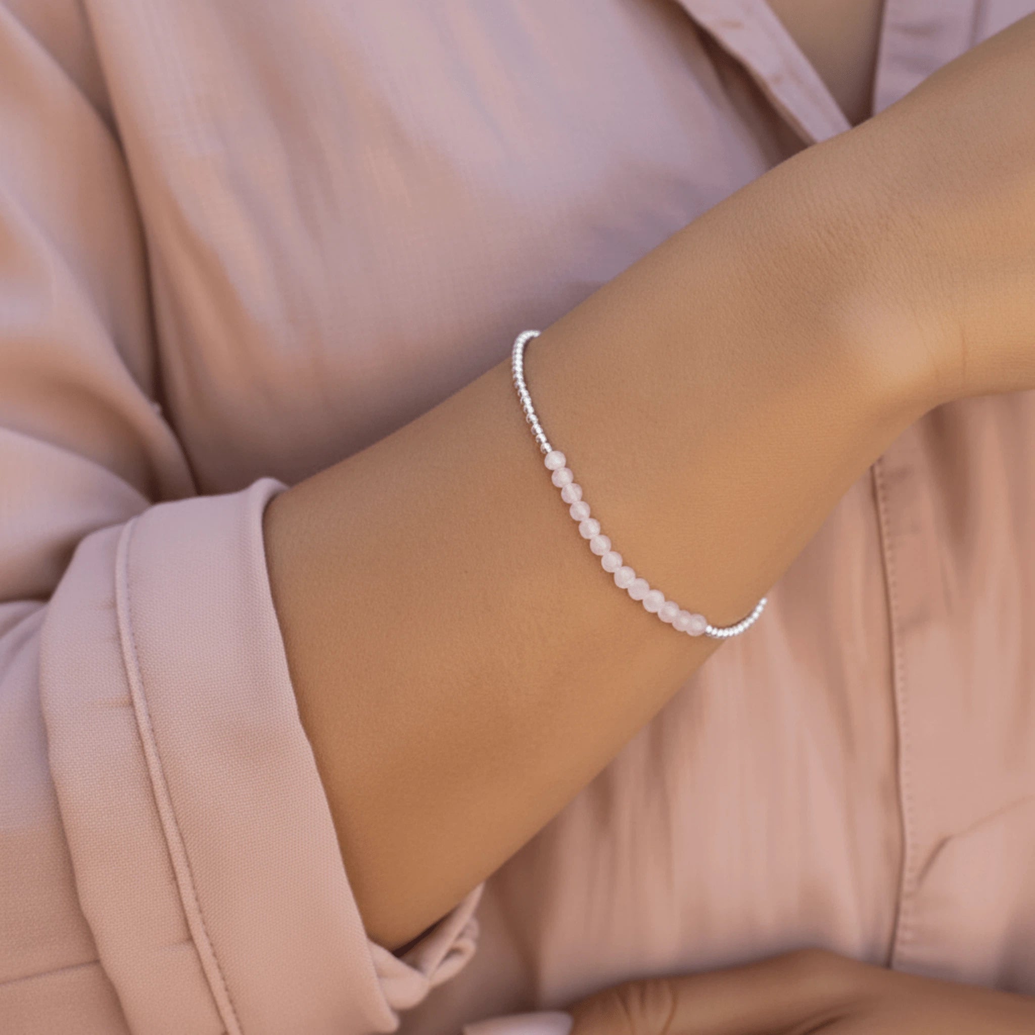 woman wearing a light pink shirt and a a sterling silver beaded bracelet with natural light pink rose quartz gemstones.