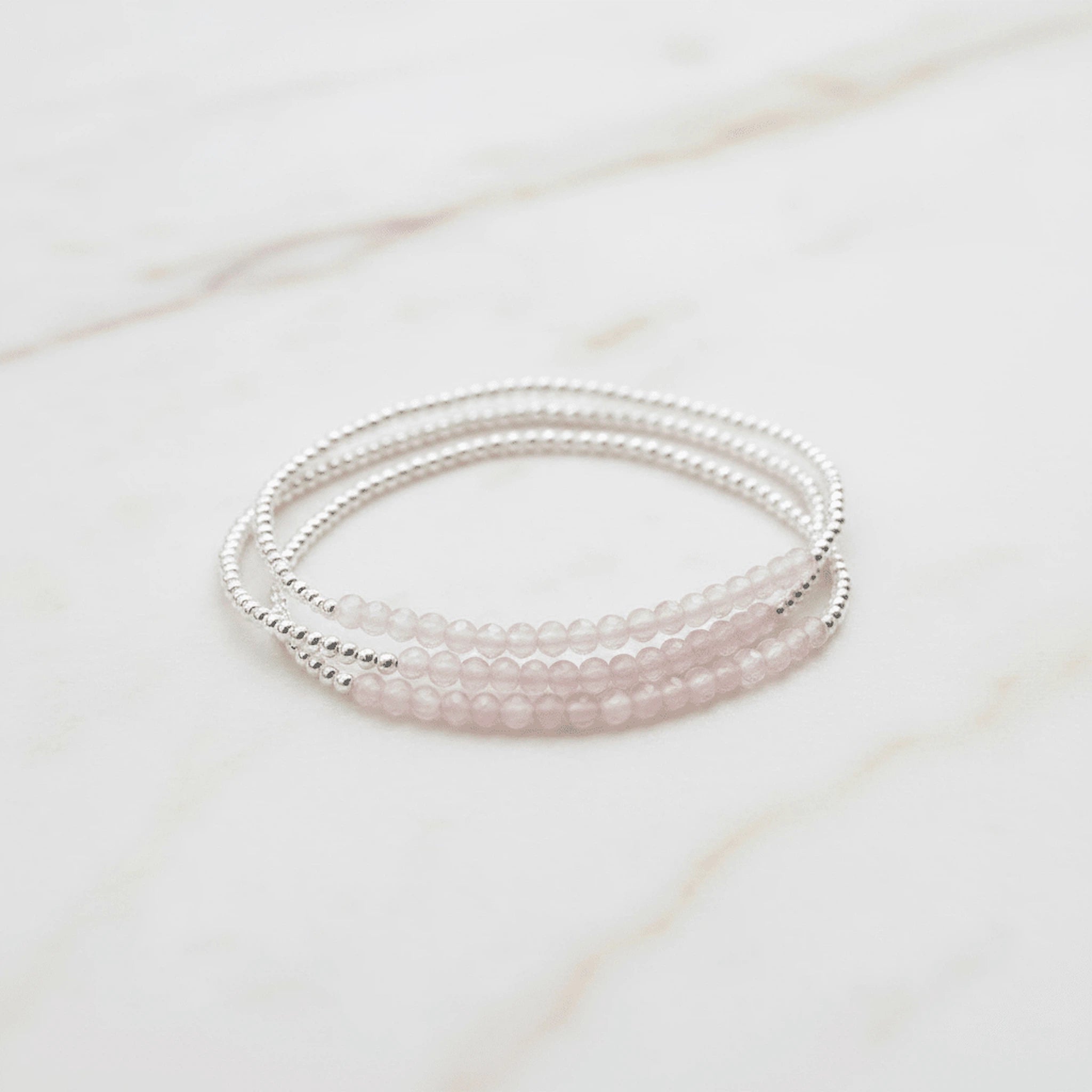 three sterling silver beaded bracelets with natural faceted light pink rose quartz gemstones on a light stone surface