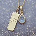 Gold necklace with a sagittarius zodiac pendant and a teardrop-shaped blue topaz gemstone on a gold and blue speckled background.