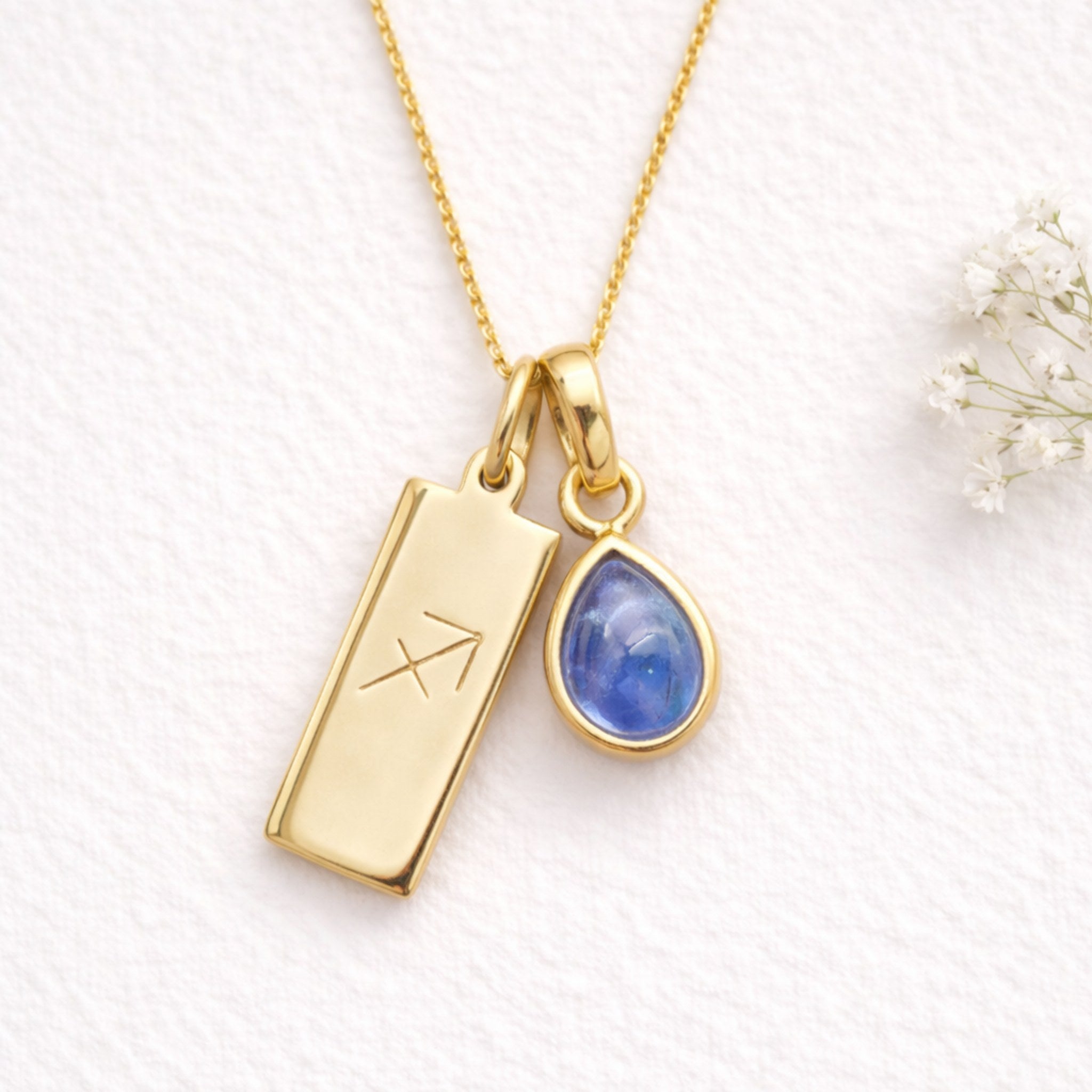 Gold Sagittarius Zodiac symbol pendant with a blue teardrop natural tanzanite gemstone on a textured white background