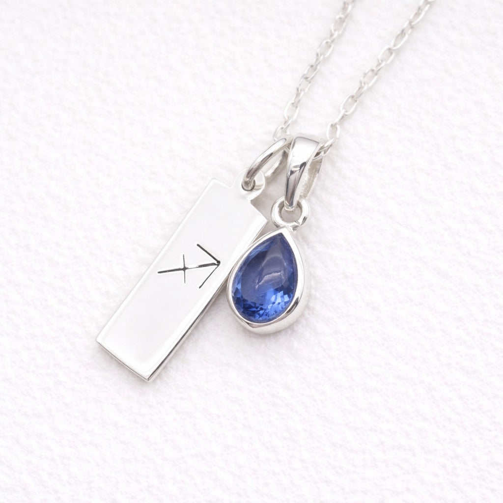 Silver sagittarius zodiac pendant necklace with a blue teardrop natural tanzanite pendant on a textured white background