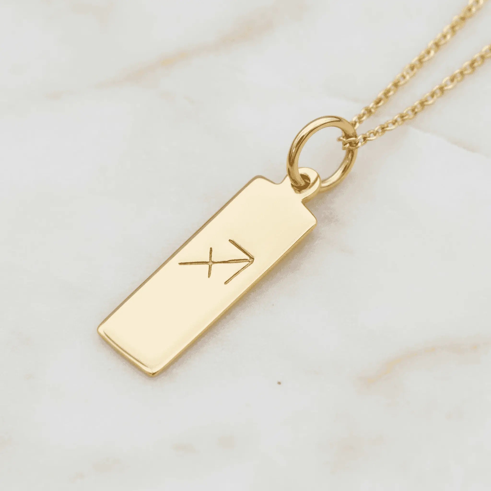 Gold necklace with a rectangular sagittarius zodiac pendant on a marble surface