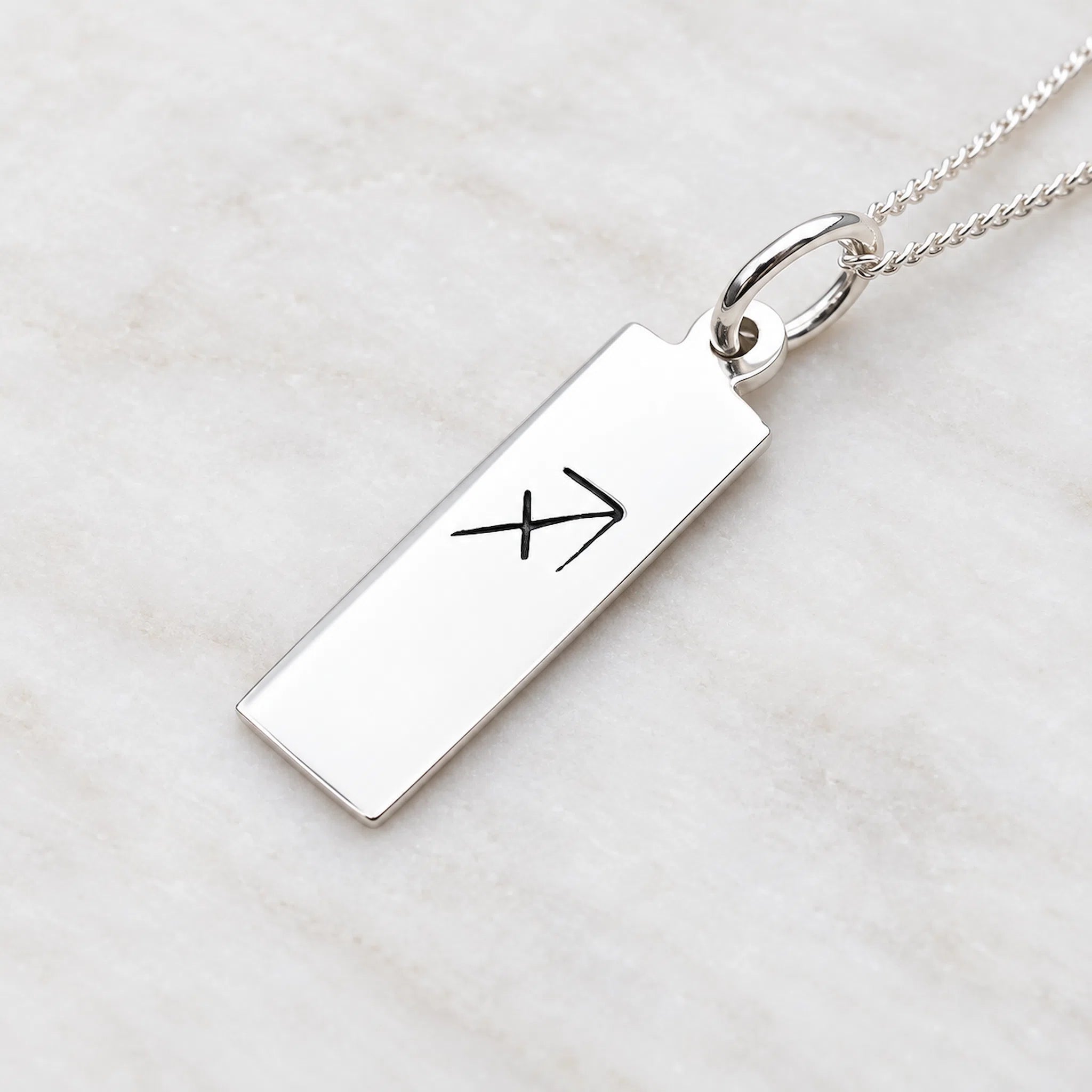 sterling silver sagittarius necklace featuring rectangle pendant engraved with minimalist sagittarius zodiac star sign line glyph symbol suspended from a fine chain on a light stone surface