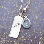 Sterling Silver necklace with a Sagittarius zodiac pendant and November birthstone blue topaz gemstone on a grey background.