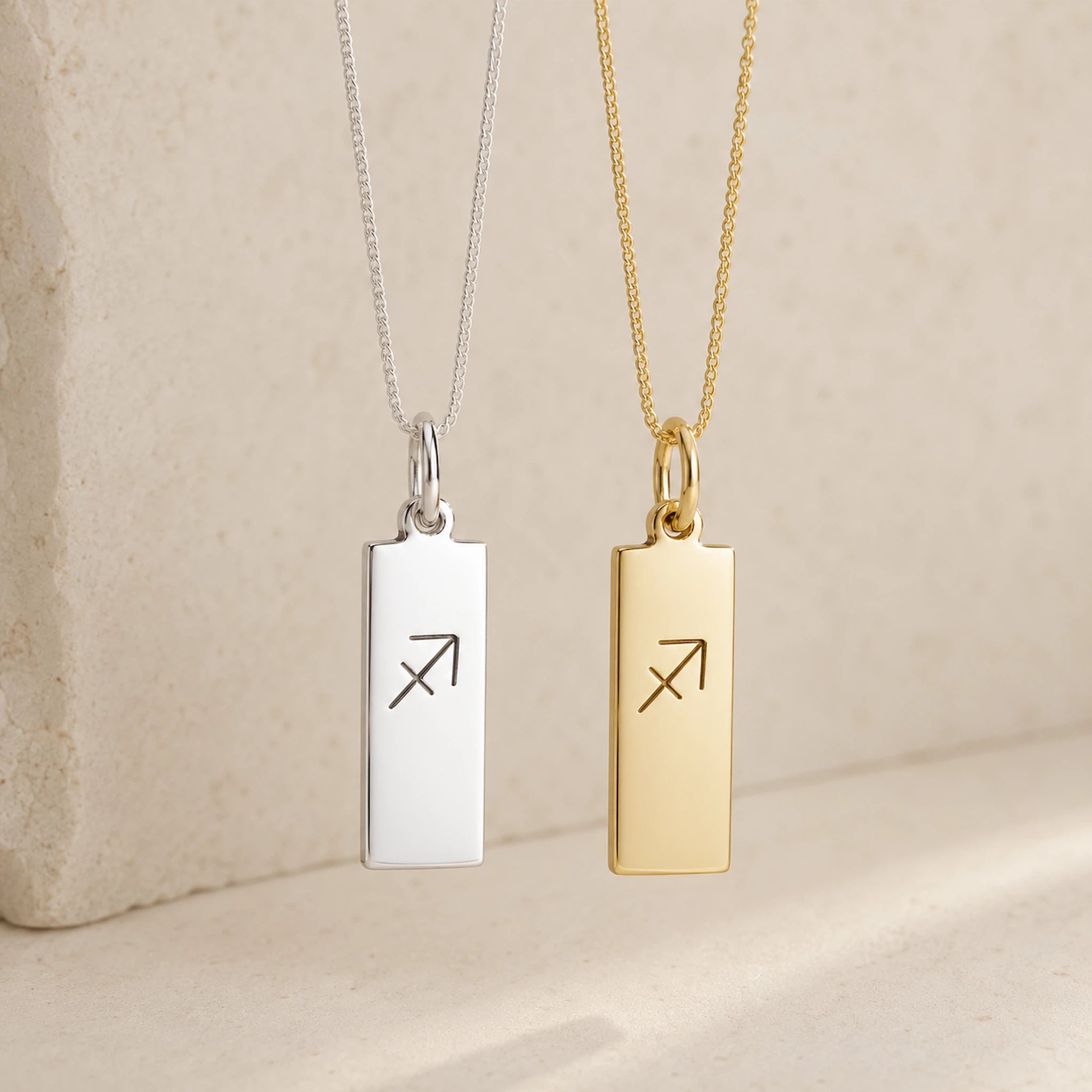 two sagittarius necklaces - fine chain silver and gold necklaces with rectangle pendants engraved with sagittarius zodiac line glyph symbol hanging.