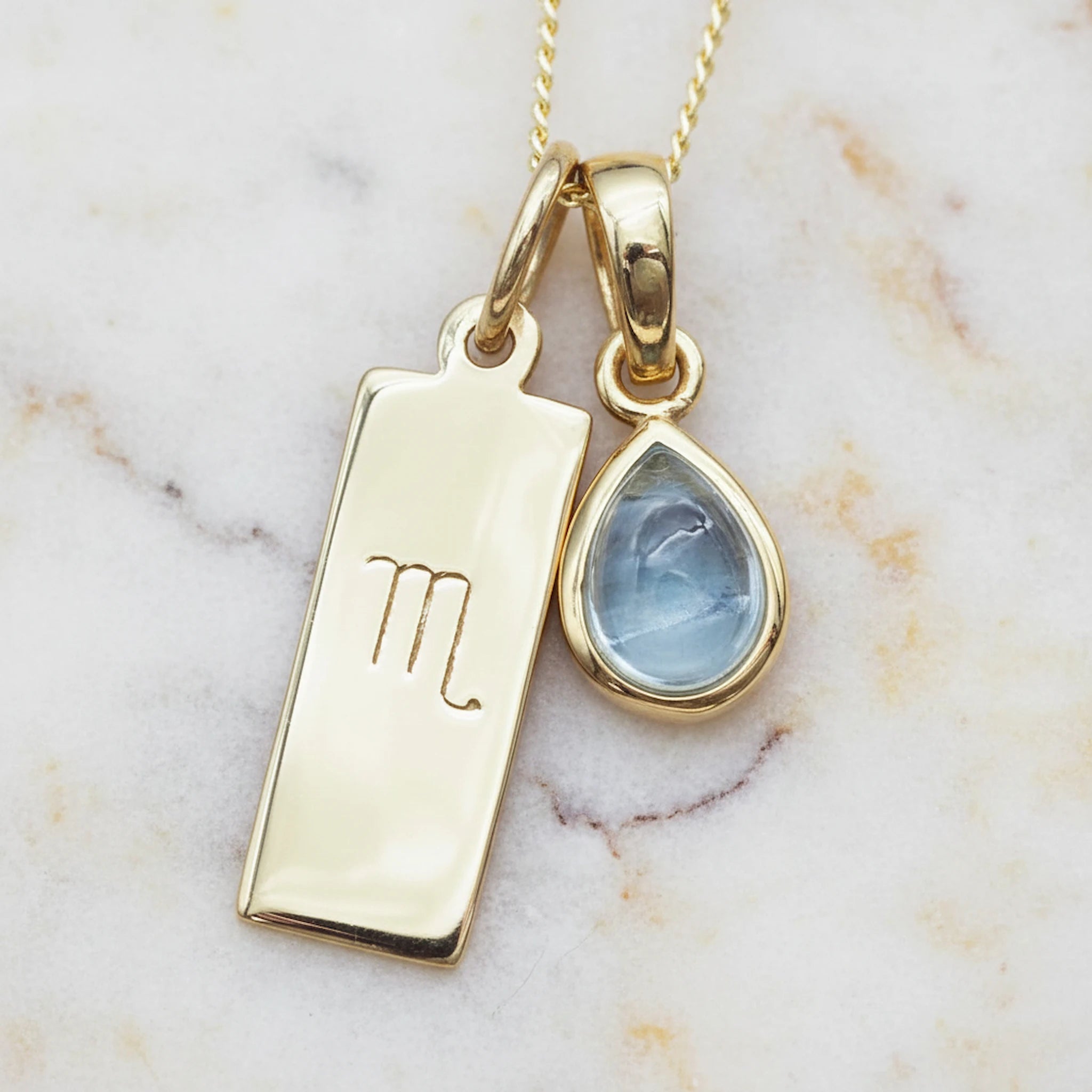 Gold necklace with Scorpio zodiac pendant and November birthstone topaz gemstone pendant on a marble background