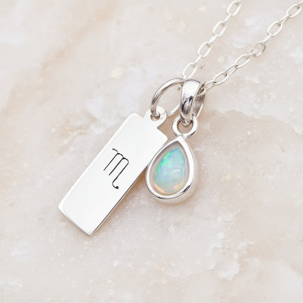 Silver necklace with a scorpio zodiac charm and opal pendant on a warm stone background