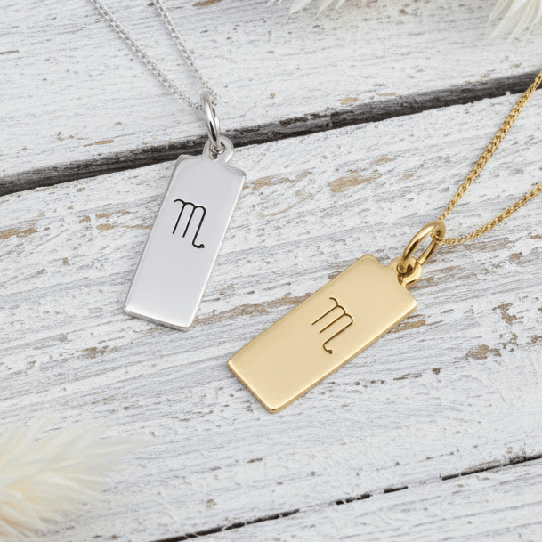 Scorpio Zodiac Necklaces in Silver and Gold laying on a wooden surface