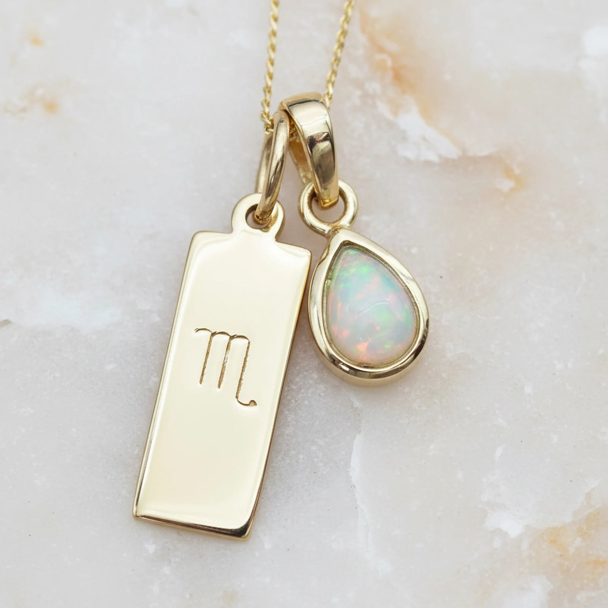 Gold Necklace with a Scorpio Zodiac Pendant and a October Birthstone Opal Pendant on a light stone background