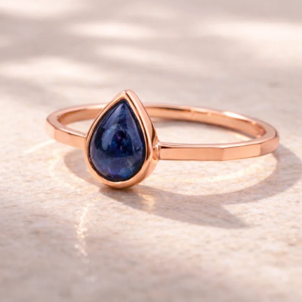 Rose gold September birthstone ring with a blue teardrop natural sapphire gemstone on a light background