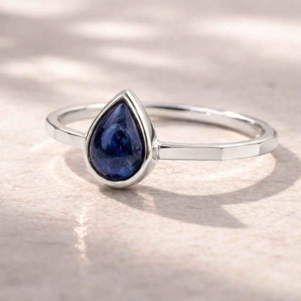 sterling Silver September birthstone ring with a blue teardrop-shaped natural sapphire gemstone on a reflective surface