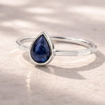 sterling Silver September birthstone ring with a blue teardrop-shaped natural sapphire gemstone on a reflective surface