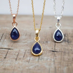rose gold, gold and silver necklaces with tear drop sapphire stones hanging above a wooden surface