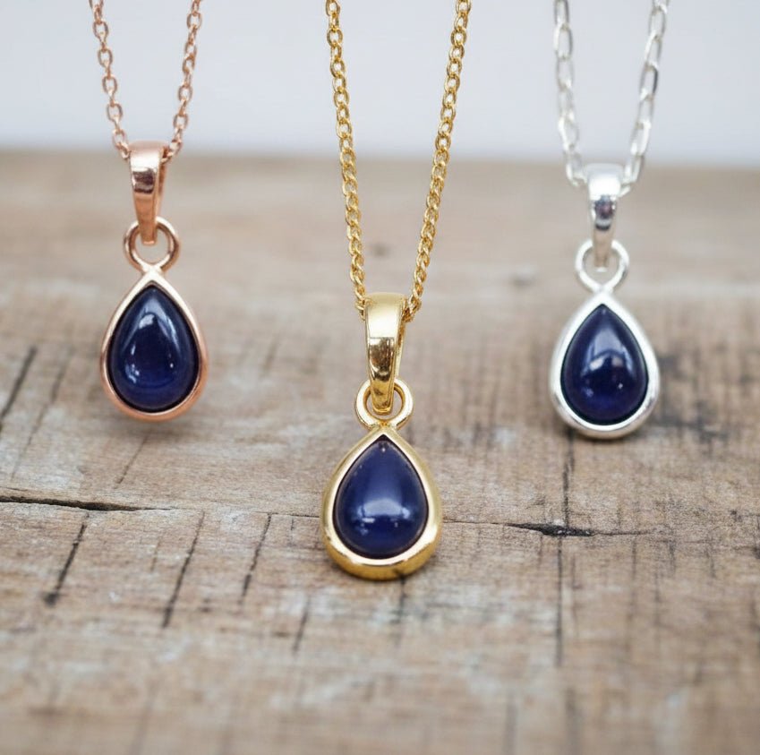 rose gold, gold and silver necklaces with tear drop sapphire stones hanging above a wooden surface