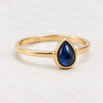 Angled gold September birthstone natural sapphire ring on a matte white surface