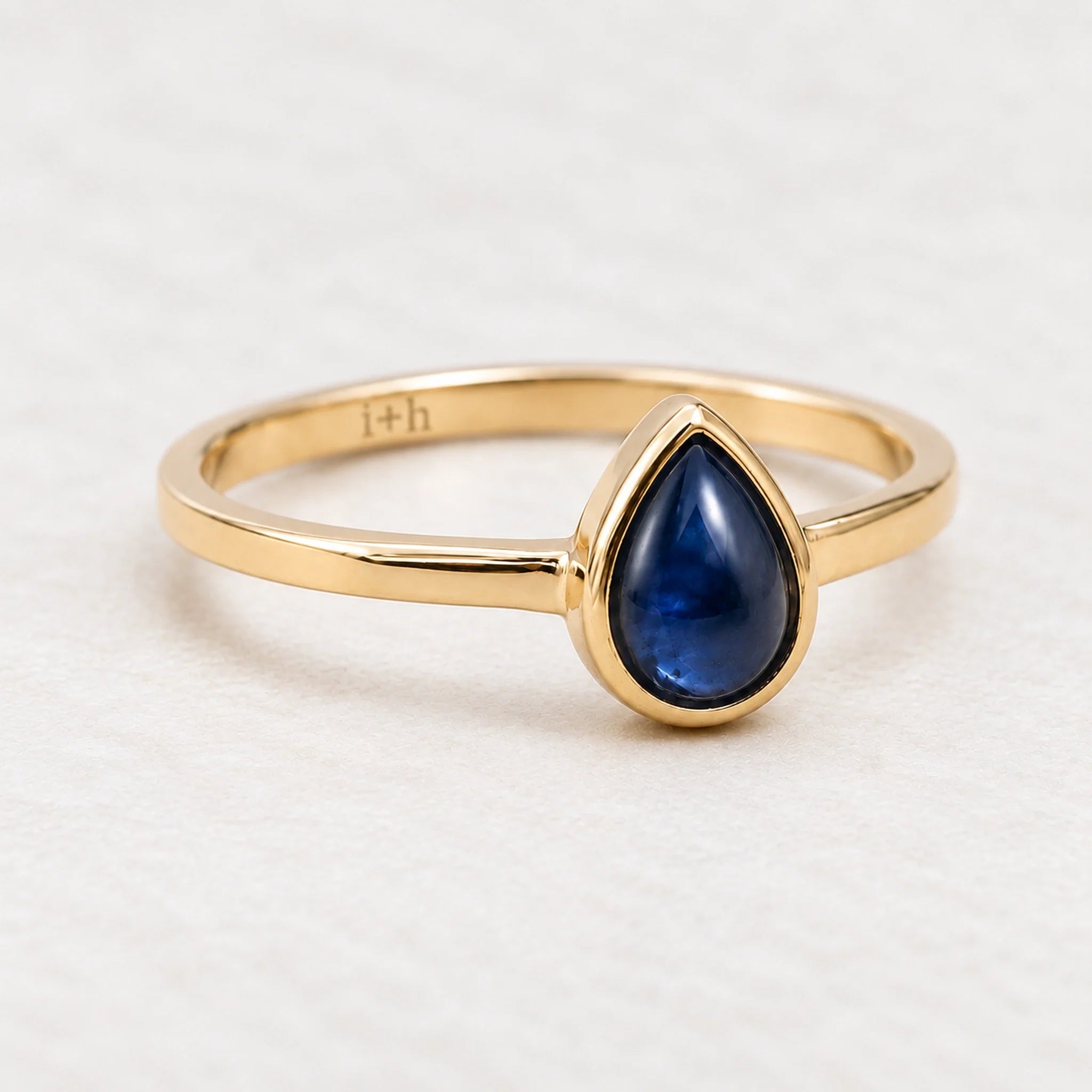 Angled gold September birthstone natural sapphire ring on a matte white surface