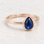 Angled rose gold September sapphire birthstone ring on a matte white surface