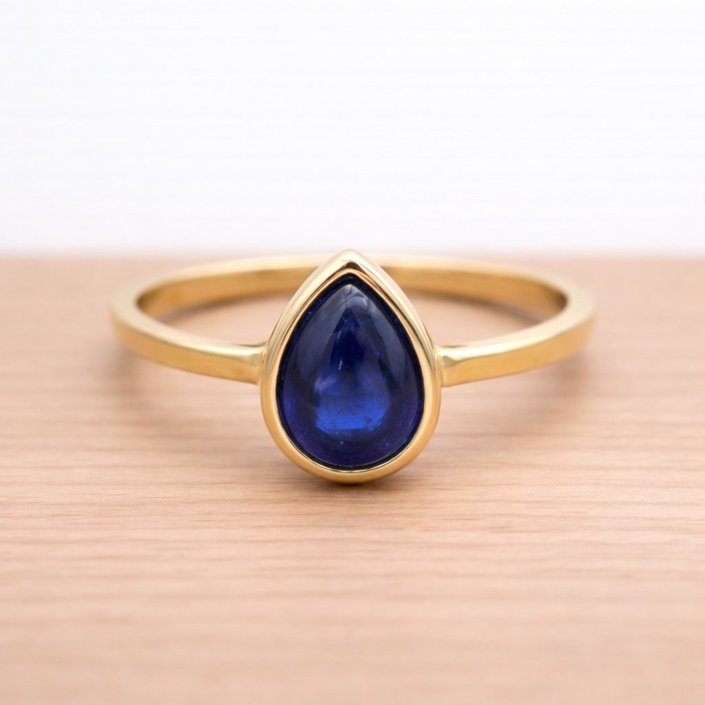 Gold ring with a blue teardrop-shaped sapphire gemstone on a wooden surface