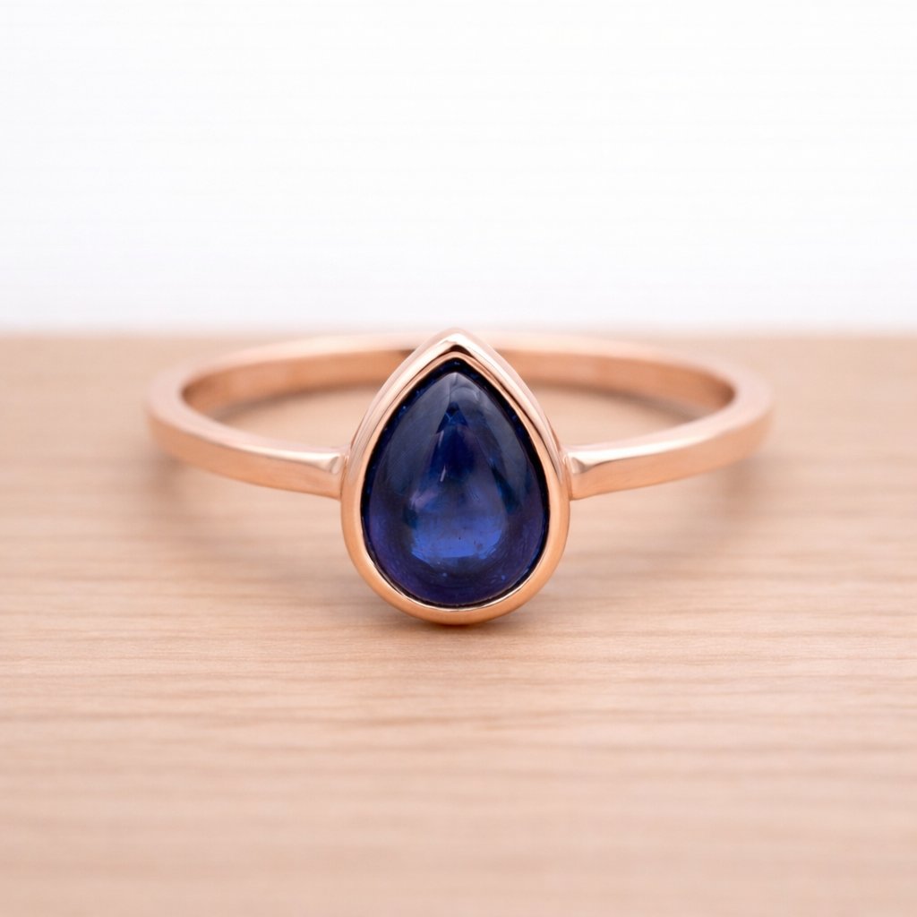 Rose gold ring with a blue teardrop natural sapphire gemstone on a wooden surface