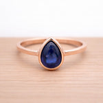 Rose gold ring with a blue teardrop natural sapphire gemstone on a wooden surface