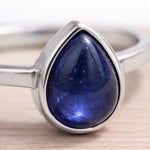 Silver ring with a blue teardrop-shaped natural sapphire gemstone on a light wooden surface