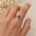 Hand wearing a gold September birthstone ring with a natural pear-shaped blue sapphire