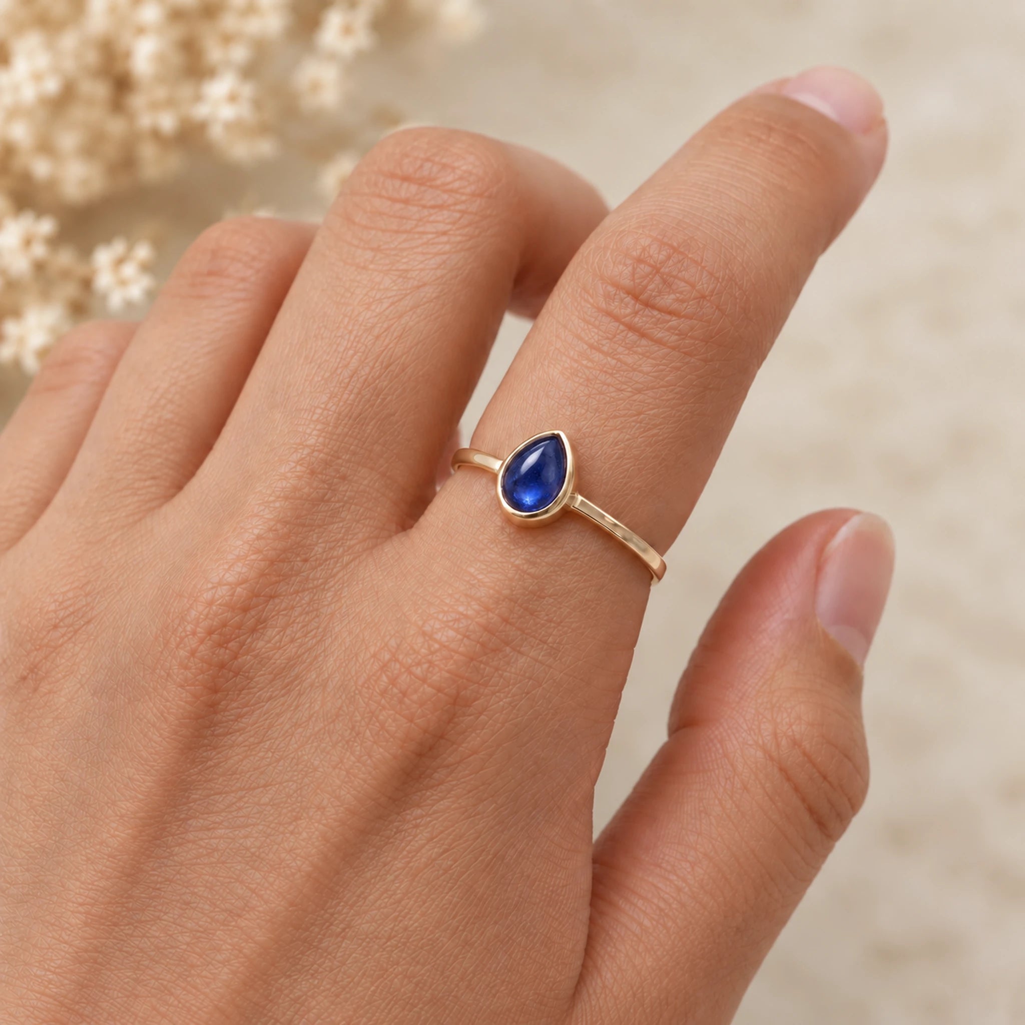 Hand wearing a gold September birthstone ring with a natural pear-shaped blue sapphire