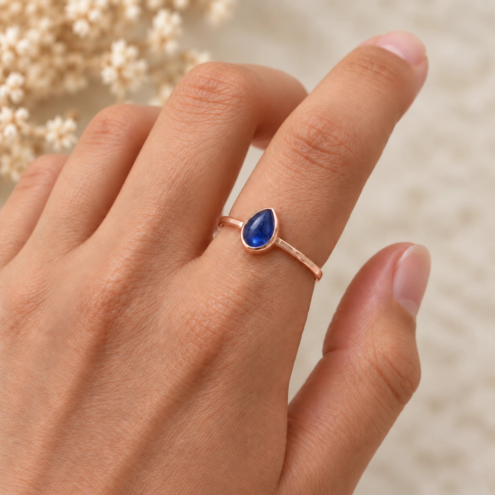 Hand wearing a rose gold September birthstone ring with a natural pear-shaped blue sapphire