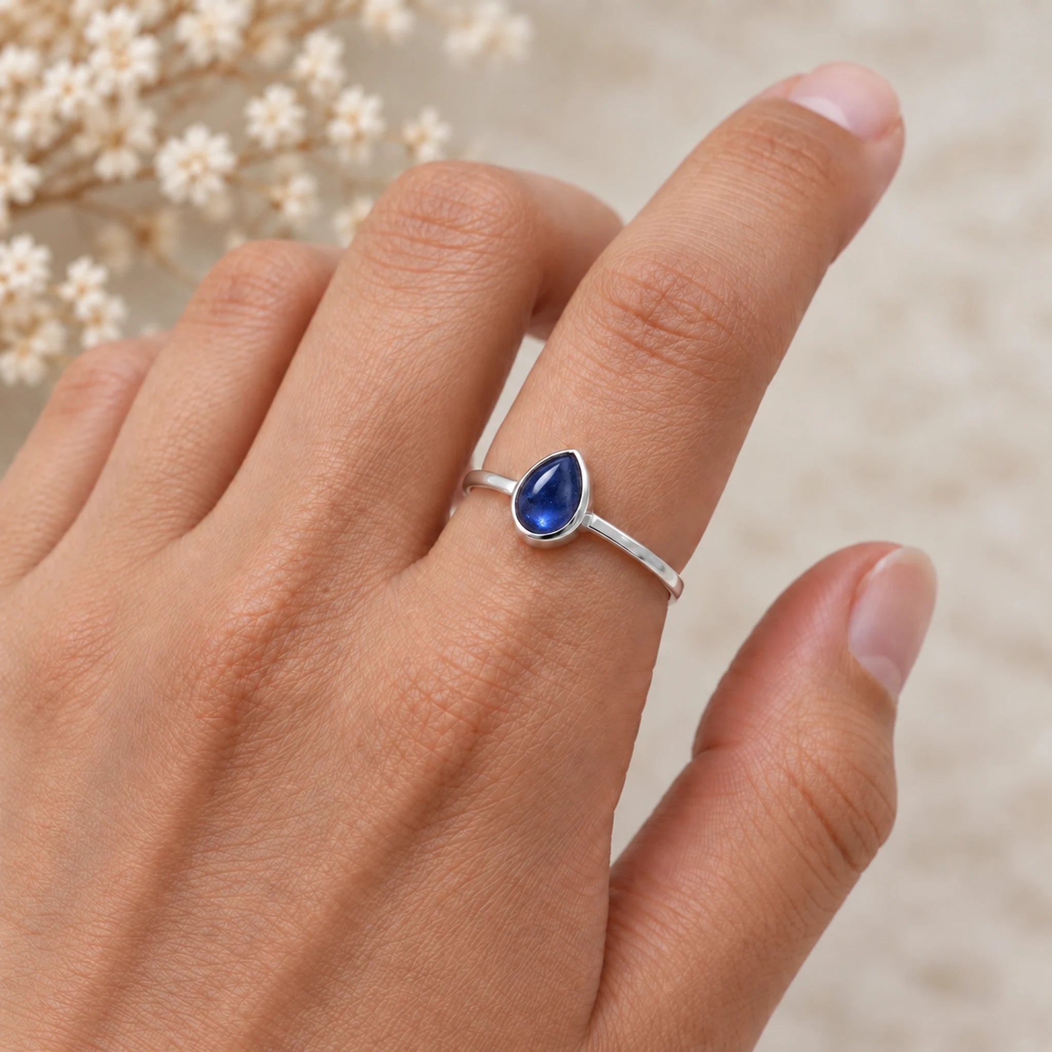 Hand wearing a silver September birthstone ring with a natural pear-shaped blue sapphire