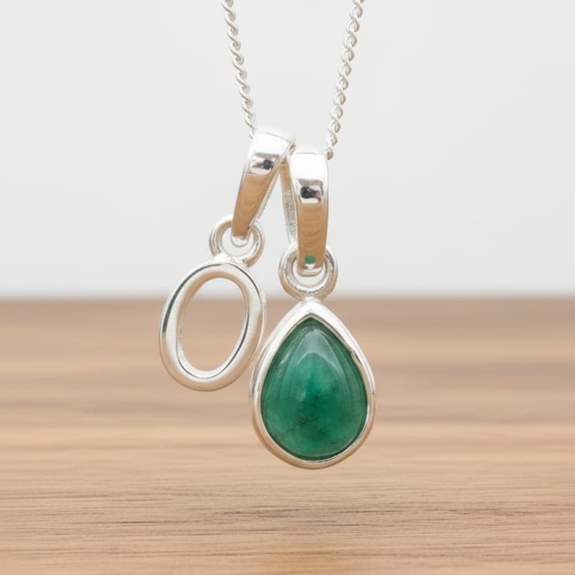 Silver Initial O necklace with a teardrop-shaped Emerald gemstone pendant hanging above a rustic wooden surface