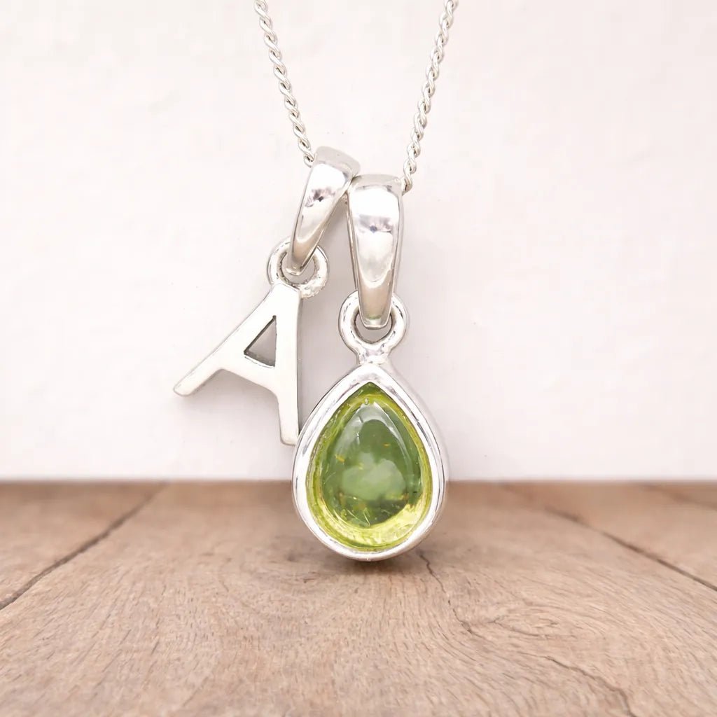 Silver necklace with a 'A' letter and a peridot teardrop pendant on a wooden surface