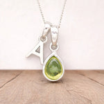 Silver necklace with a 'A' letter and a peridot teardrop pendant on a wooden surface