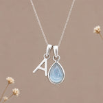 Sterling silver initial A and November natural blue topaz necklace on a taupe background with sparse ivory flowers