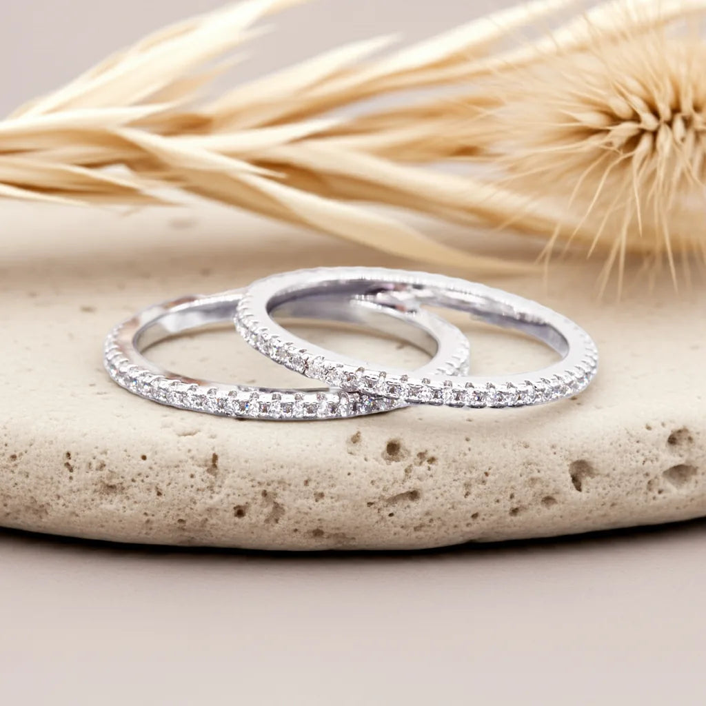 Two silver rings with small stones on a stone surface with dried plants in the background