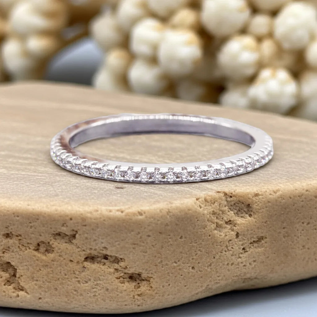 Silver ring with small diamonds on a stone surface with blurred pearls in the background