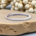 Silver ring with small diamonds on a stone surface with blurred pearls in the background