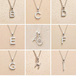 Collection of silver letter necklaces A to I on a beige background as initial options for a personalised April Birthstone Clear Quartz Necklace.