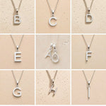 Collection of silver letter necklaces A to I on a beige background as initial options for a personalised April Birthstone Clear Quartz Necklace.