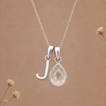 sterling silver initial j april birthstone natural clear quartz pendant necklace against a dark warm beige background